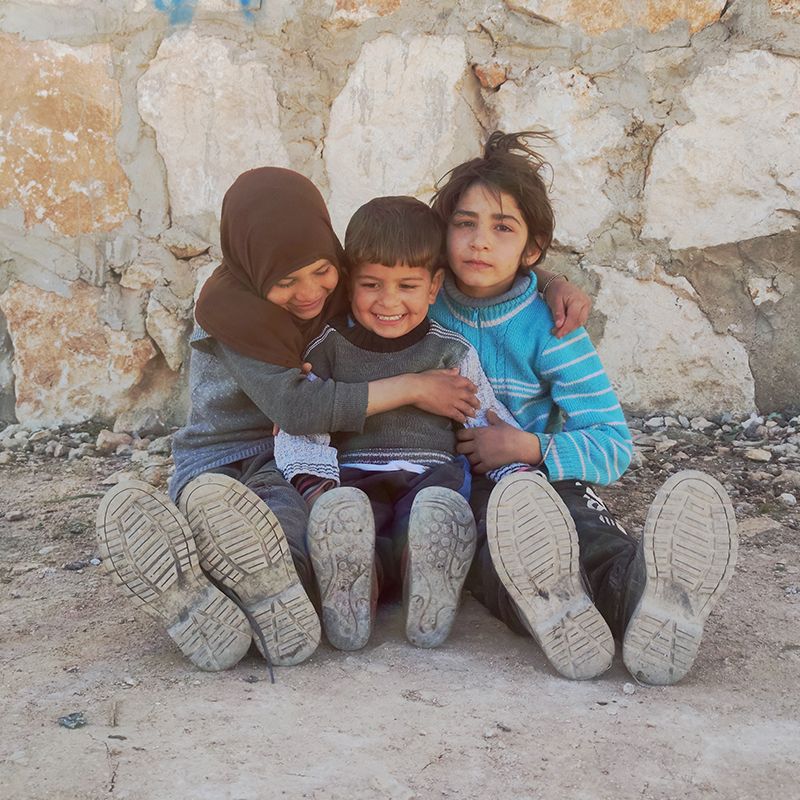 Three smiling children in a camp for people displaced by the ongoing Syria conflict in Kelly, Idleb, Northwestern Syria