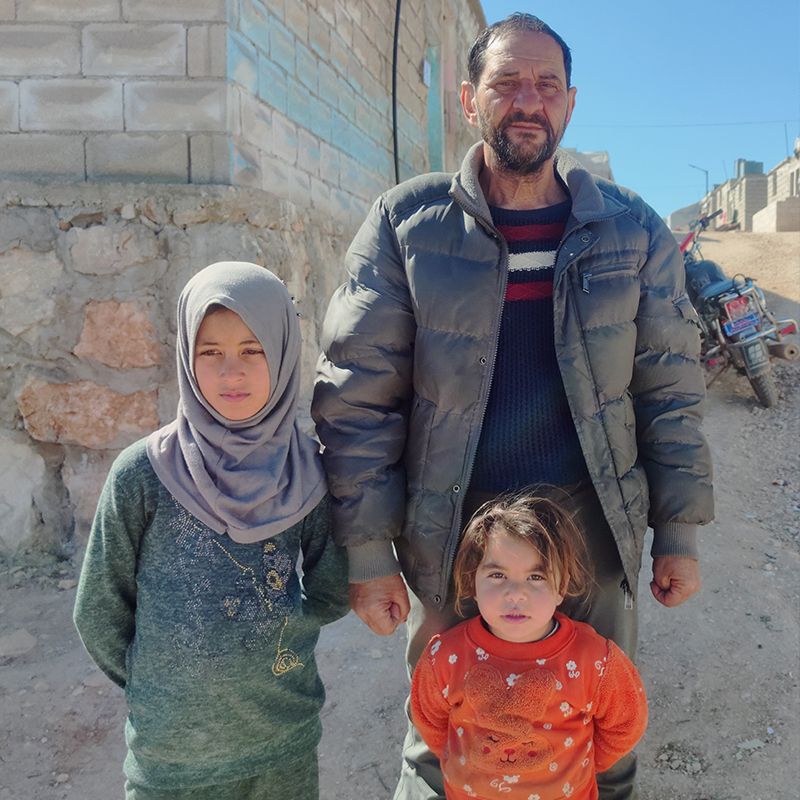 A man standing with his two daughters at a camp for displaced people in Kelly, Idleb, Syria
