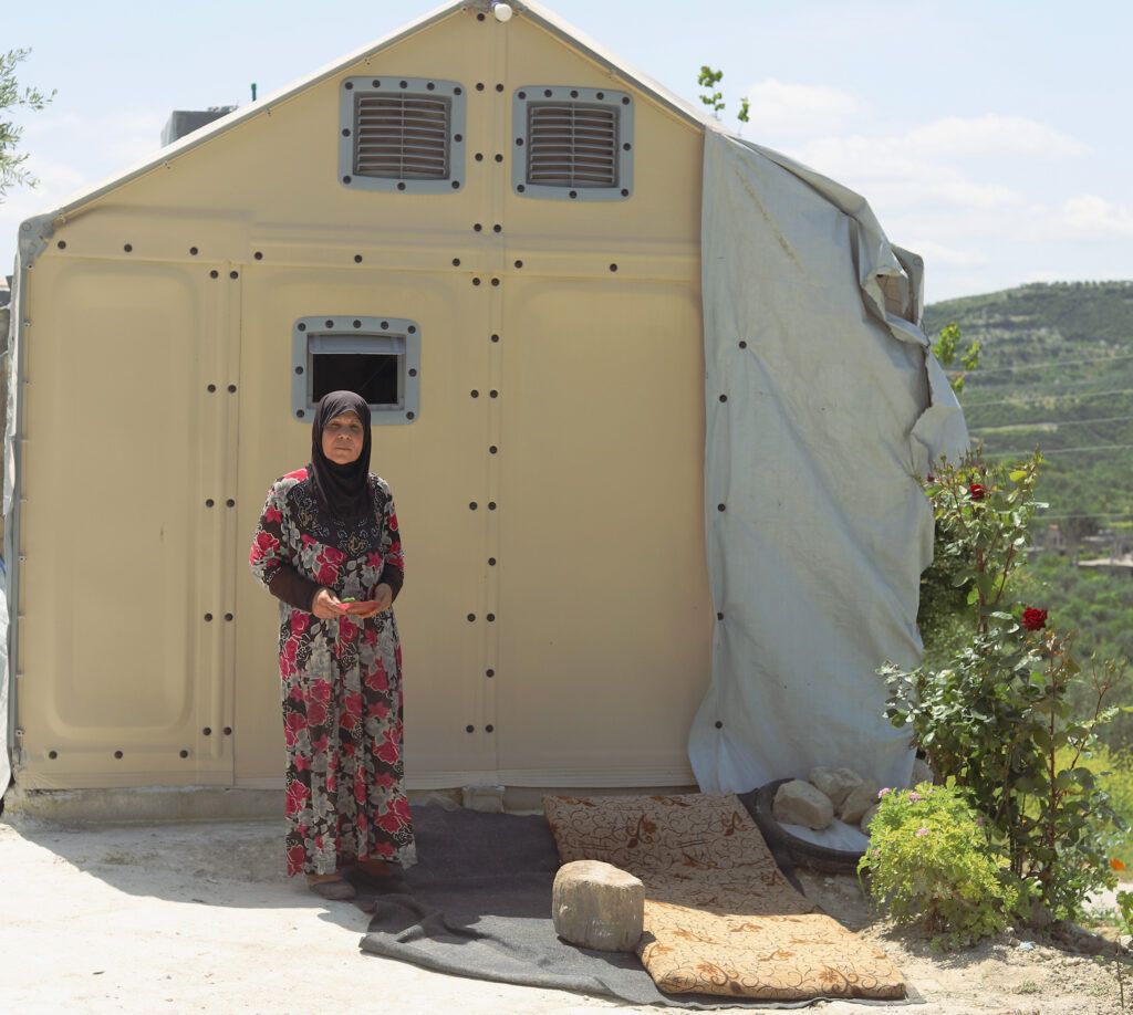 Um Rahman in front of her family’s Relief Housing Unit. Photo: Idleb, Syria. April 2024.