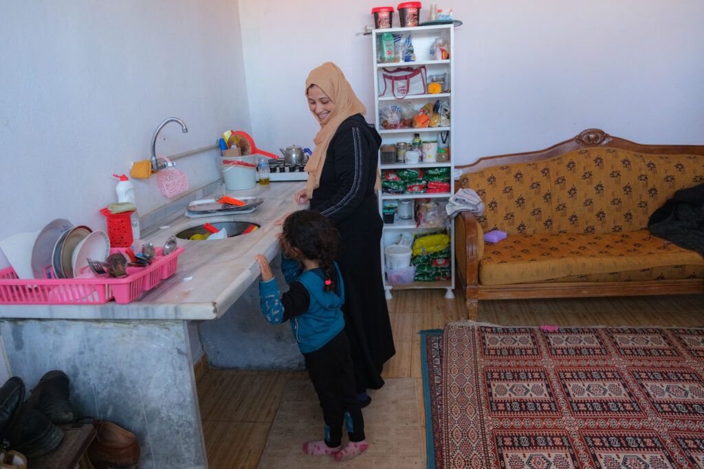 Aisha and her young daughter smile as they use aid delivered by GOAL.